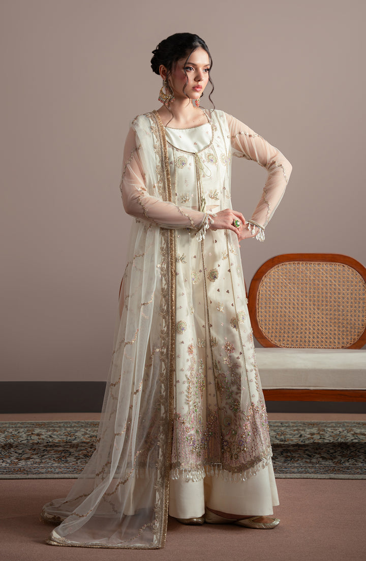 Woman wearing a traditional outfit with a floral design in a room with a beige wall and wooden chair.