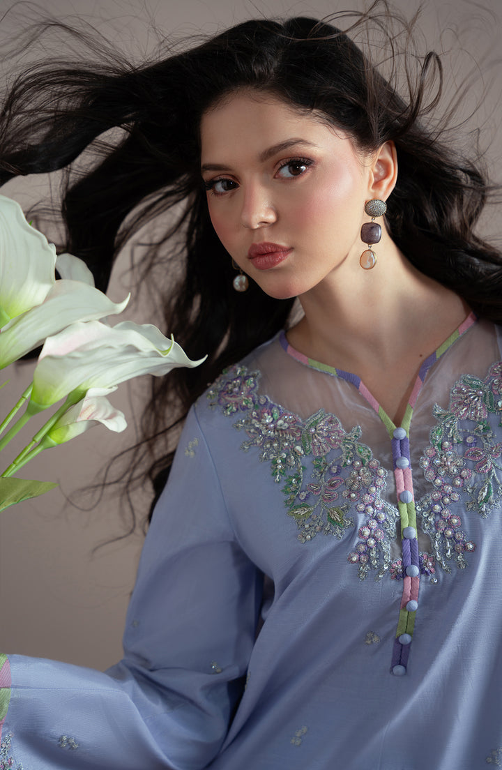 Woman wearing a light blue embroidered traditional outfit with flowers in the background