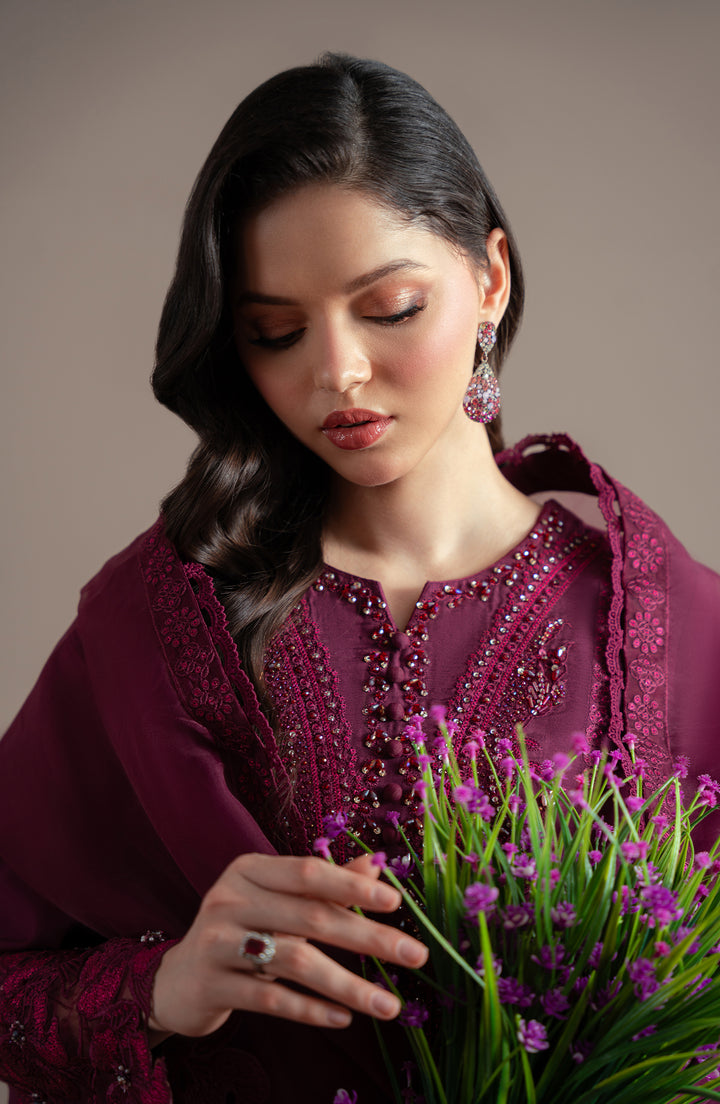 Woman in a purple traditional outfit holding a bouquet of purple flowers against a neutral background