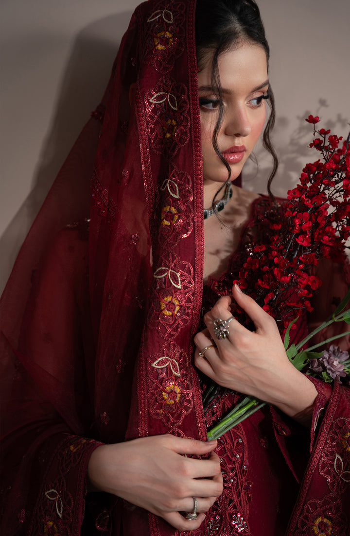 Woman in a red embroidered garment holding flowers against a neutral background